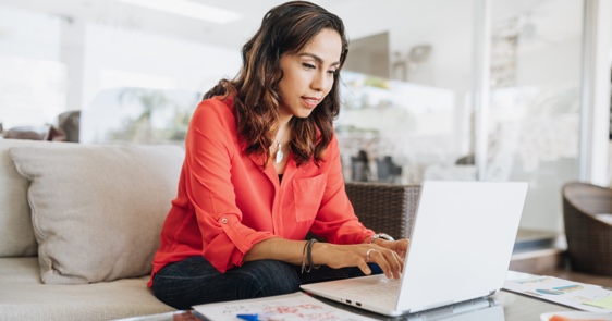 Photo d’une femme assise sur un divan qui travaille sur son ordinateur portable 