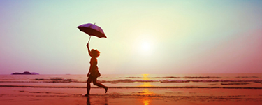 Femme court sur la plage au coucher du soleil en tenant un parapluie
