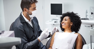 Photo d'un dentiste avec masque et d'une patiente souriant sur le fauteuil dentaire