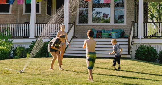 Enfants jouent dans un jet d’eau sur une pelouse