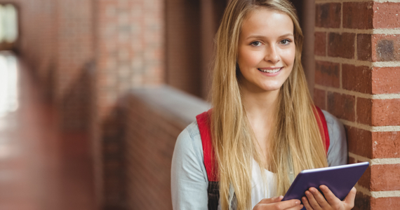 Jeune étudiante dans un couloir d’université tient une tablette en souriant