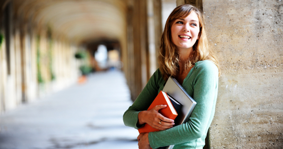 Jeune femme sur un campus universitaire sourit en tenant ses livres dans ses bras
