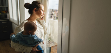 Femme avec un bébé dans ses bras parle au téléphone en regardant par la fenêtre