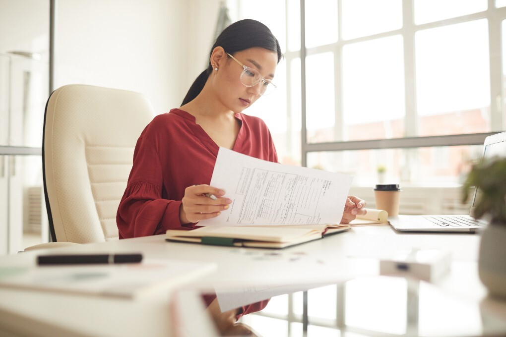 Image d’une femme regardant des documents assise à son bureau