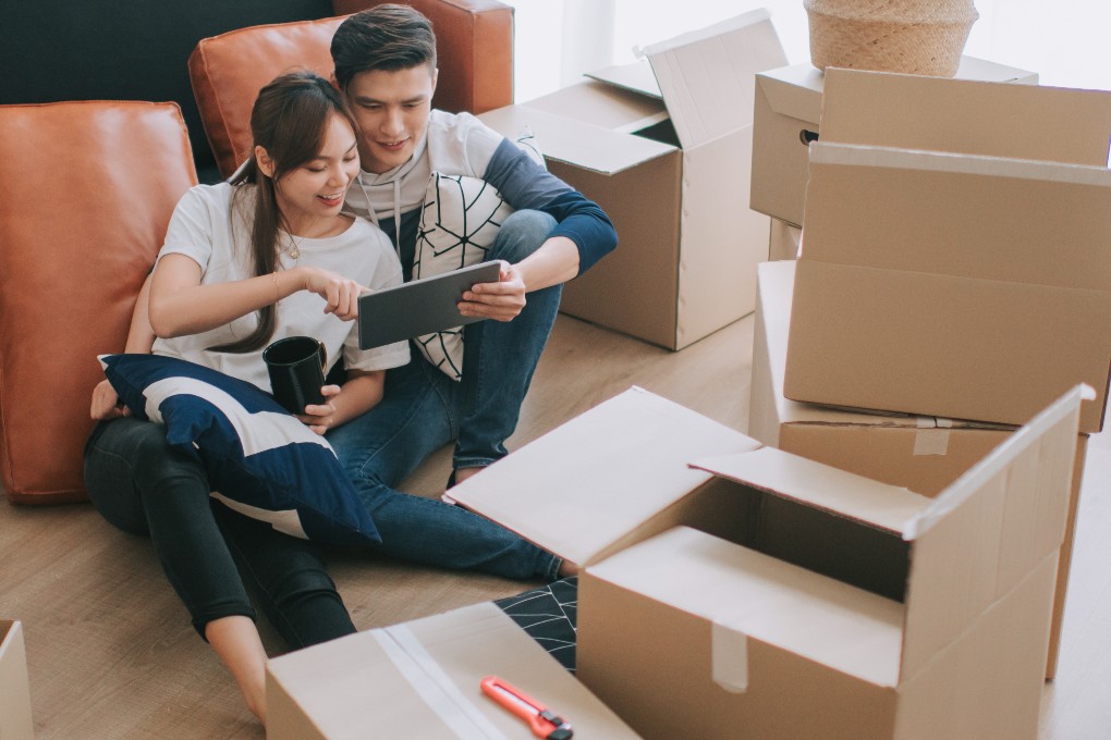 Un jeune couple prépare son déménagement entouré de boîtes de carton dans leur salon lumineux.