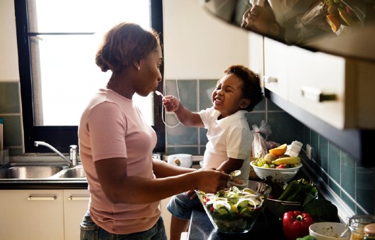 Un enfant donne à manger à sa mère pendant qu’elle cuisine.