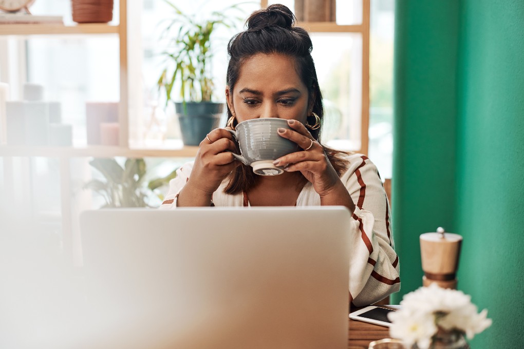Image d'une jeune femme buvant un café devant son ordinateur