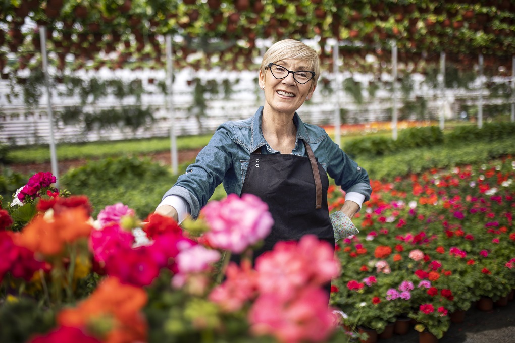Une femme travaillant dans une serre remplie de fleurs sourit à la caméra.
