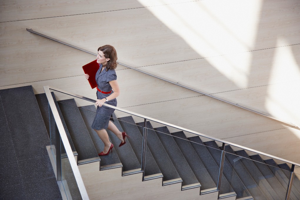 Photo d’une femme montant un grand escalier moderne, un cartable à la main 