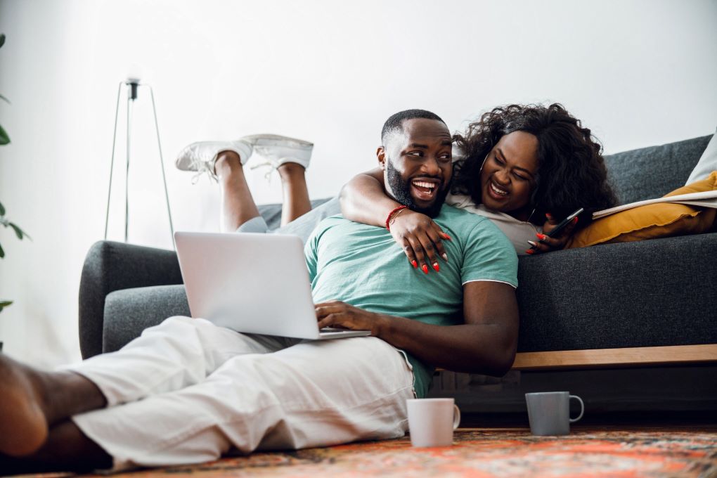Photo d’un homme et d’une femme qui rient en consultant un ordinateur portable dans leur salon