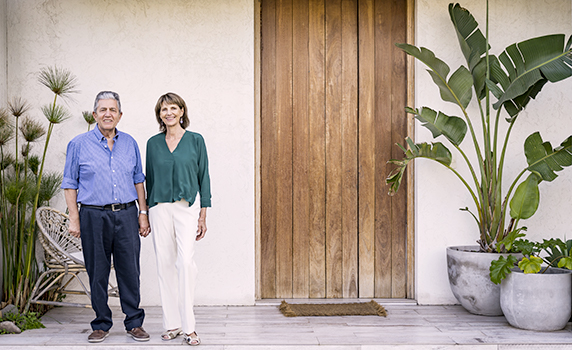 Photo d’un couple debout devant une villa en Floride avec une grande porte en bois et des plantes tropicales