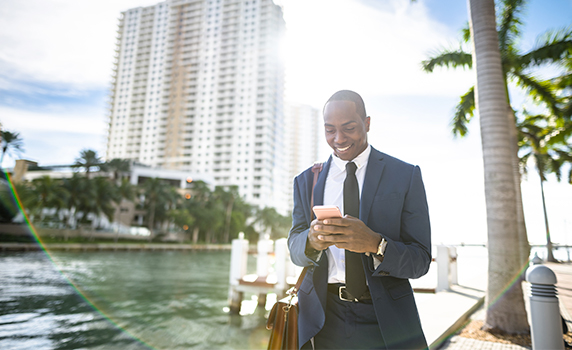 Photo d’un homme en complet consultant son téléphone cellulaire près d’une tour à logements au bord de la mer en Floride