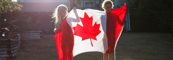 Photo of two children holding the Canadian flag in a sunny backyard