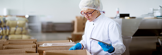 Photo d’une femme en sarrau vérifiant des boîtes dans une usine de transformation alimentaire
