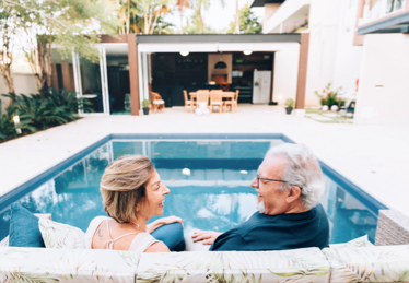 Photo d’un couple de retraités discutant sur le bord d’une piscine bordée de palmiers en Floride