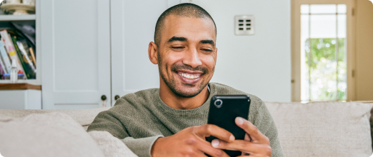 Photo d’un homme souriant en consultant son téléphone mobile dans son salon
